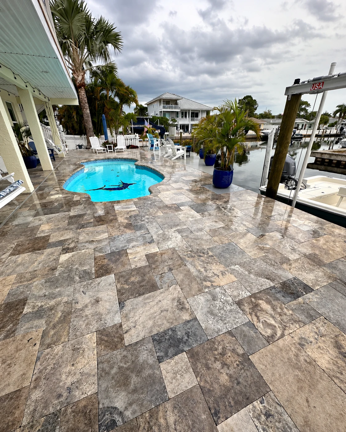 Wide view of the patterned pool deck, freeform pool, palm planters and adjoining boat dock.